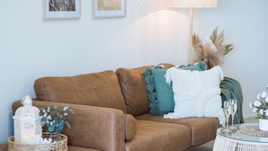 Ein braunes Ledersofa mit dekorativen Kissen, einem weißen Laternen und einem kleinen Tisch mit Glasplatte.