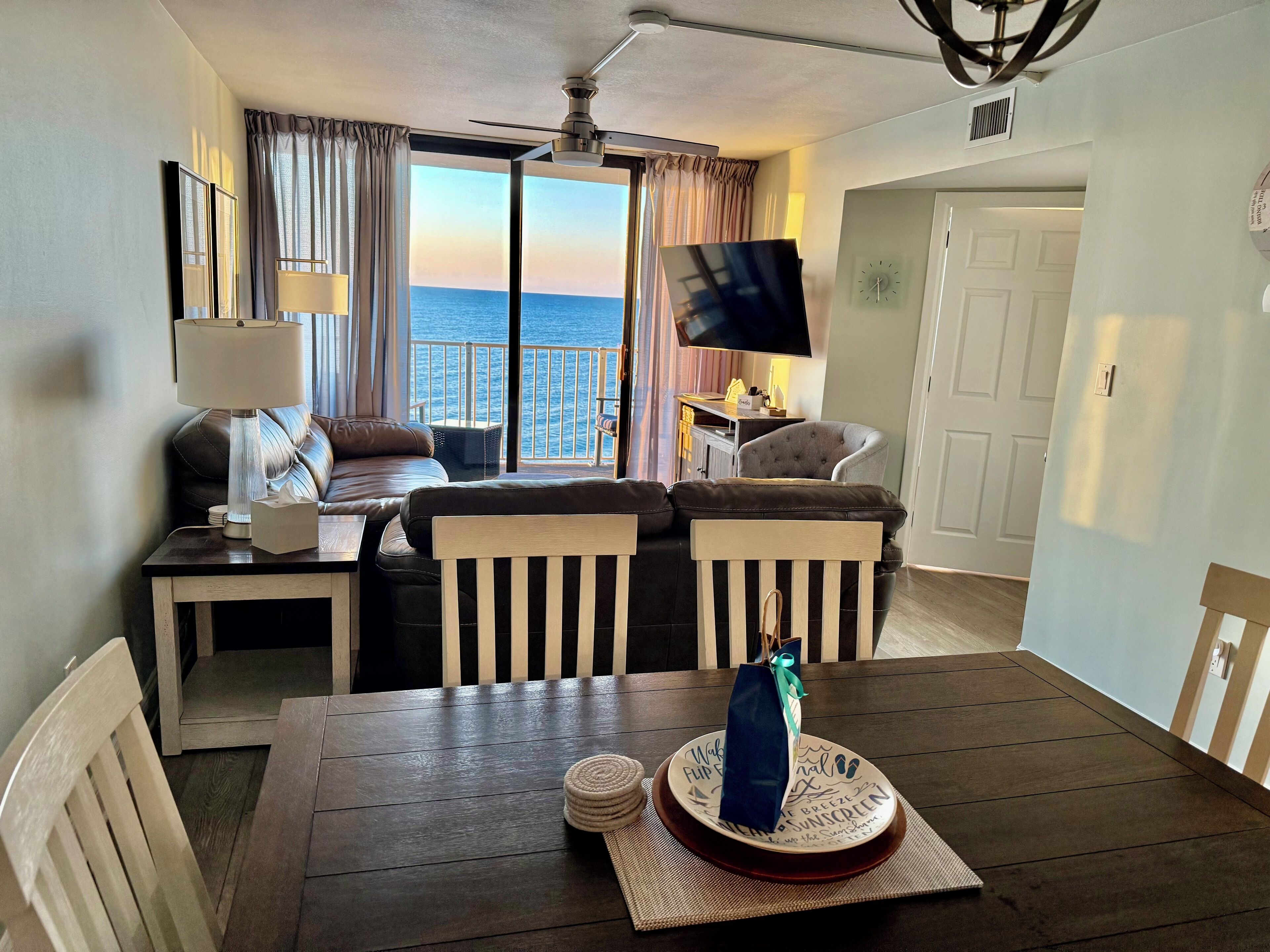 A modern living room with a view of the sea, a flat-screen TV, and a dining area with a table and chairs.