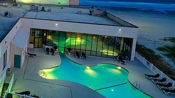 Un área de piscina con sillones de descanso y un edificio con paredes de vidrio.