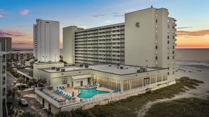 Un hotel con piscina en la azotea, varios balcones y vista al mar.