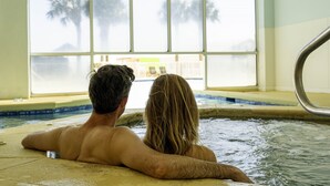 Een koppel ontspant in een jacuzzi met uitzicht op palmbomen en een gebouw door een groot raam.