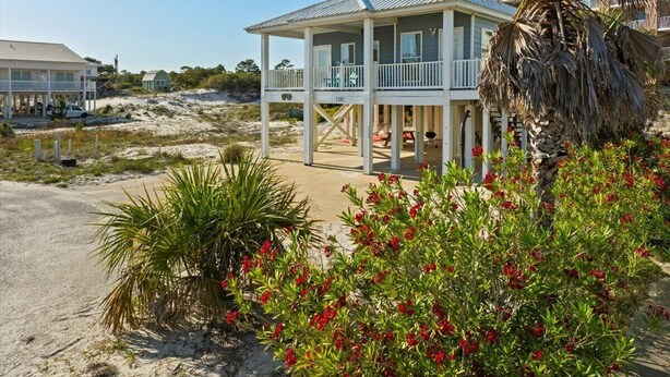 Een huis aan het strand met een overdekte veranda, een zandstrand op de achtergrond en tropische begroeiing voor.