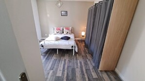 Quarto com cama, mesa de cabeceira, luminária e cortina.