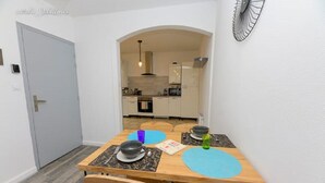 Uma sala de jantar com mesa de madeira, quatro cadeiras e cozinha ao fundo.