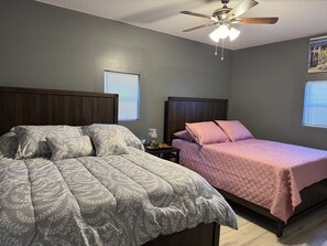 Une chambre avec deux lits, un ventilateur de plafond et une fenêtre avec des stores.