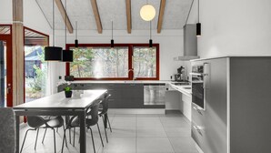 Een moderne keuken met een centraal eiland, roestvrijstalen apparatuur en een groot raam met zonwering.