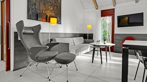 Een moderne woonkamer met een grijze bank, een bijzondere stoel, een eettafel en een tv aan de muur bevestigd.
