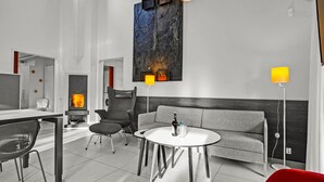 Een moderne hotelkamer met een bank, een ronde tafel, een stoel, een open haard en een groot abstract schilderij aan de muur.