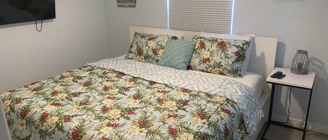 A bedroom with a floral-patterned bedspread, a television on the wall, and a bedside table with a lamp.