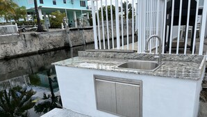 Un pequeño espacio de cocina al aire libre con un lavamanos y un armario, junto a un elemento decorativo de agua.
