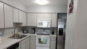A compact kitchen with white cabinets, a stainless steel sink, a microwave, a stove, and a refrigerator. - Tampa two bedroom, two bathroom Lakehouse II (Tampa)
