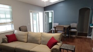 A living room with a beige sofa, red cushions, a small table, and a dining area with chairs. - Tampa two bedroom, two bathroom Lakehouse II (Tampa)