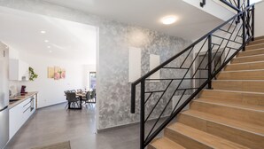 A modern kitchen with a dining area, a staircase with black railings, and a textured wall. - Gorgeous home in Rijeka (Rijeka)