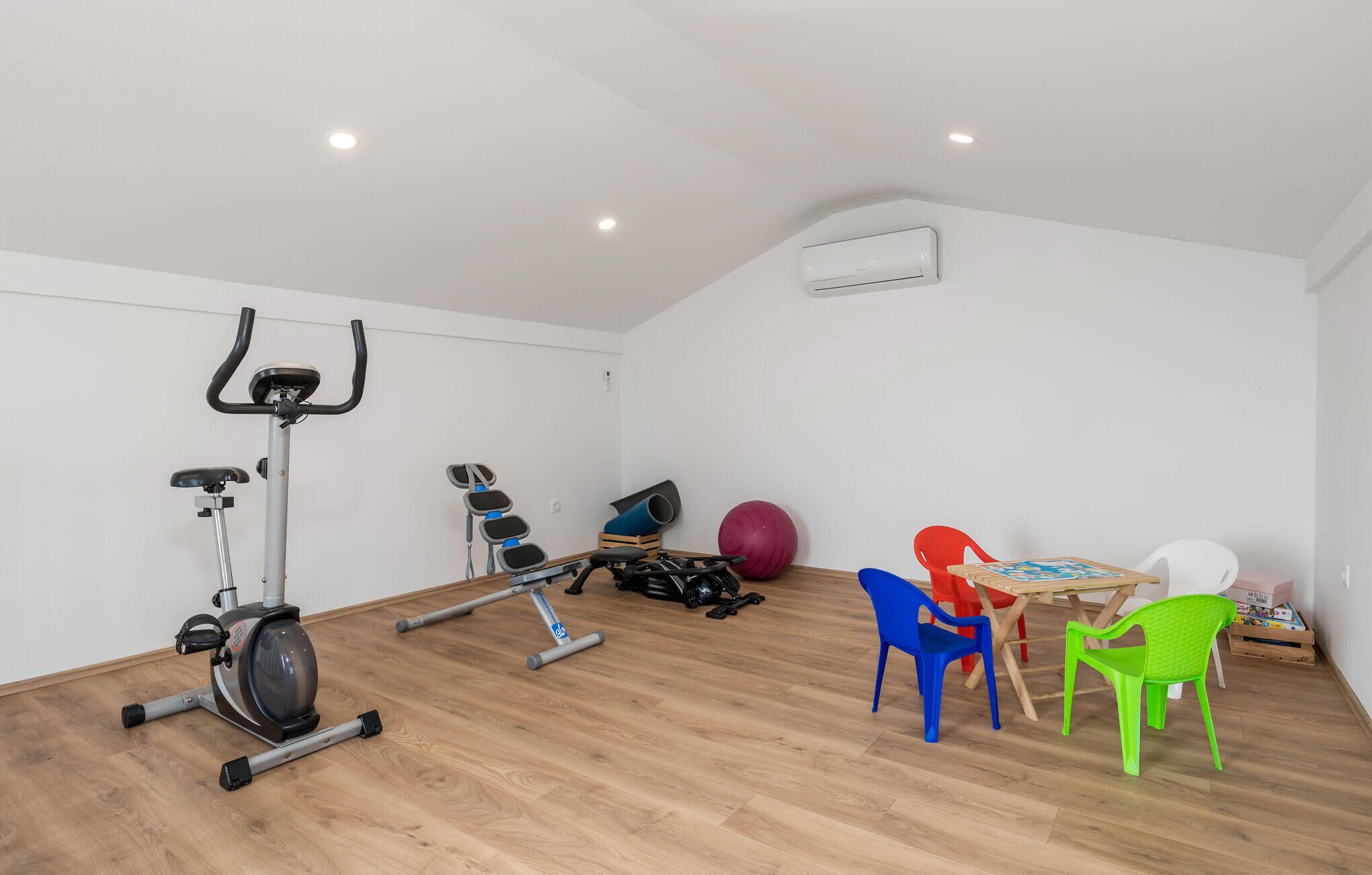 Ein Zimmer mit einem Crosstrainer, einem kleinen Tisch mit Stühlen und einem großen Gymnastikball.