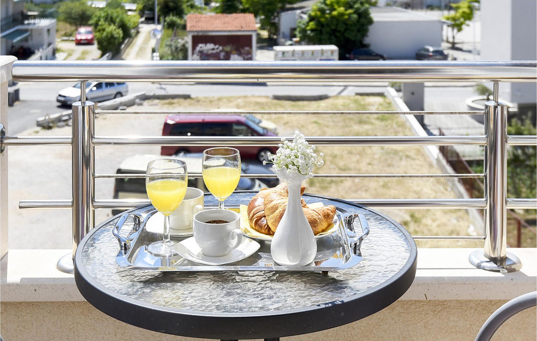 Une table de balcon sur laquelle se trouve un plateau avec un croissant, deux verres de jus d’orange et une tasse de café.