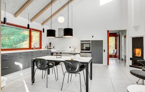 A modern kitchen with a central island, two pendant lights, and a view of a garden through a window.