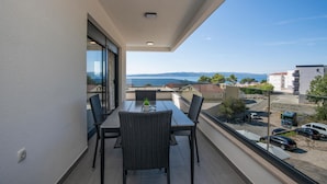 Un balcon avec une table et des chaises, offrant une vue sur la côte, avec des bâtiments et des voitures garées.