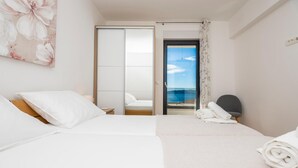 Une chambre d’hôtel avec un lit, une chaise et une vue sur la mer, visible par la porte.