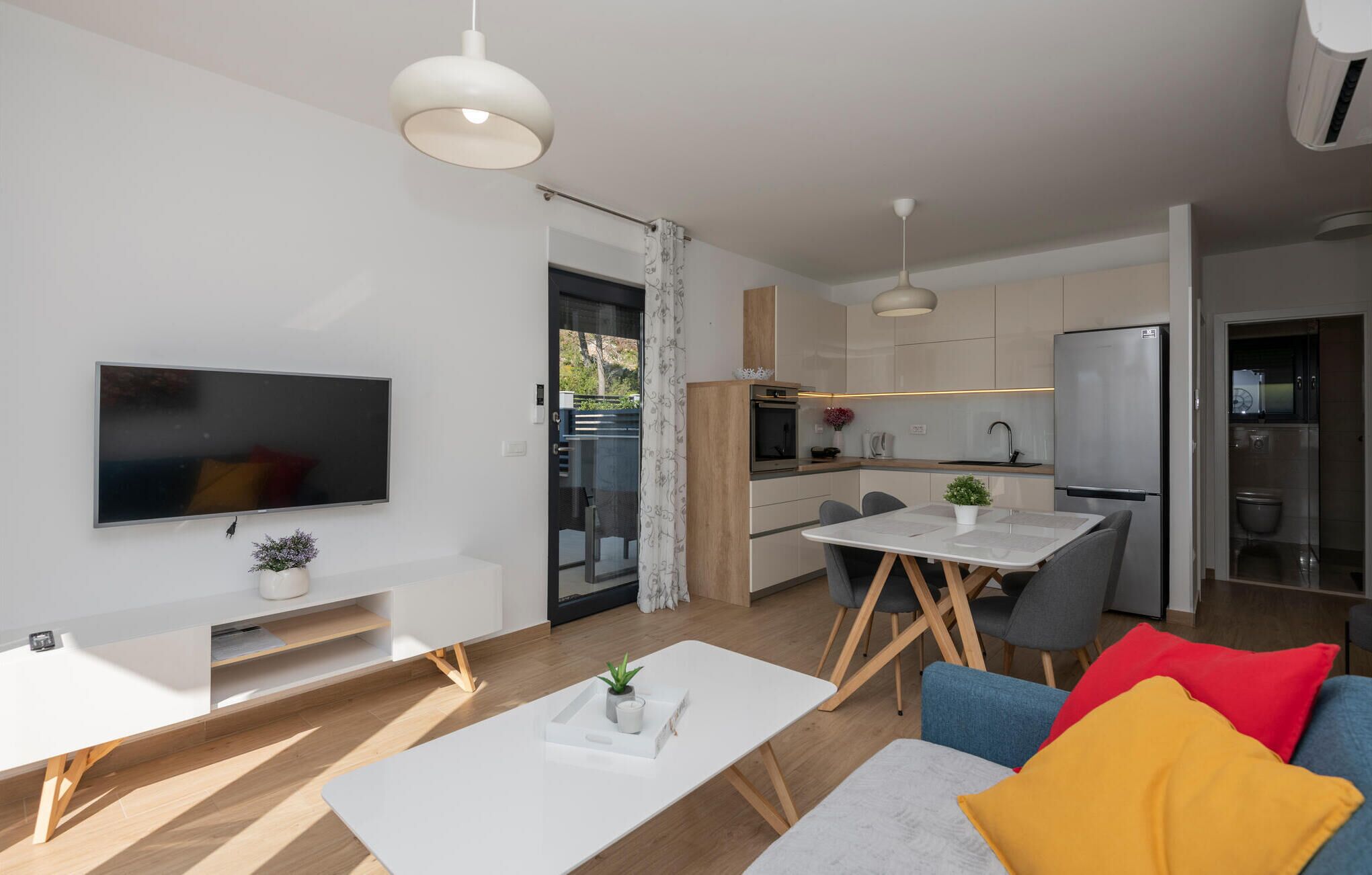 A modern apartment with a living area, a dining table, a kitchen, and a TV.