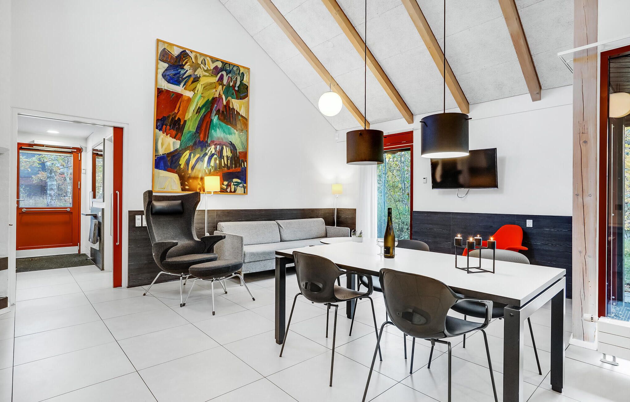 Un espace repas moderne avec une table blanche, des chaises noires et un grand tableau abstrait accroché au mur.