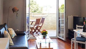 Una sala de estar con un sofá, una mesa de centro de vidrio, un televisor y un ventanal corredizo que da a un área exterior con una silla y una mesa.