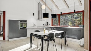 A modern kitchen with a dining area, featuring a large window with a view of trees, a built-in oven, and pendant lighting. - Lovely home in Grenaa with kitchen (Grenaa)