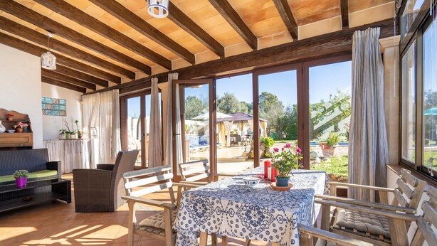 An open-plan living area with a wooden ceiling, large windows, a table with a patterned tablecloth, and outdoor seating. - Luxurious home in Sineu (Sineu)