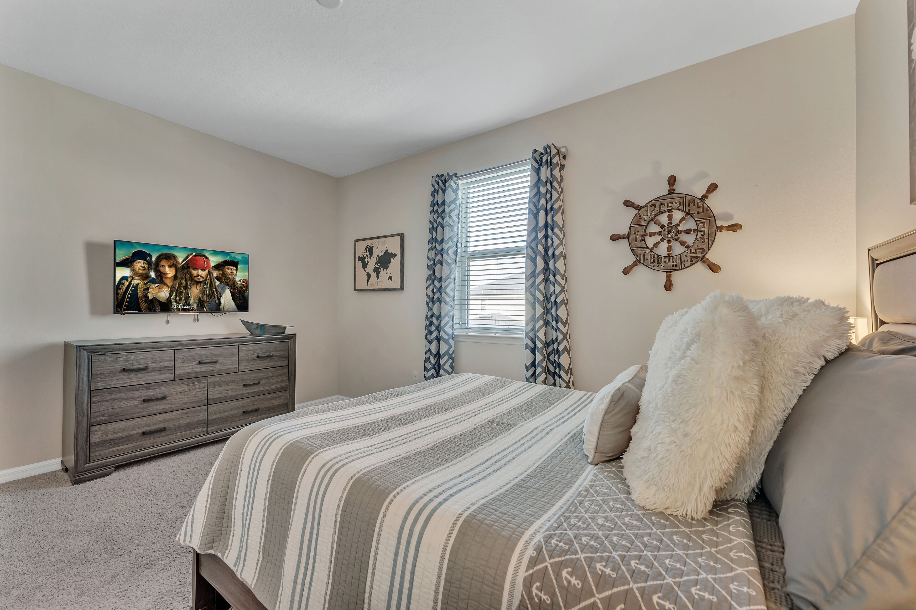 A bedroom with a bed, a dresser, a wall-mounted ship's wheel, and a painting.
