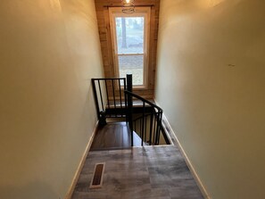 Una escalera estrecha con barandilla de madera y metal, que lleva a una ventana con vistas a árboles.