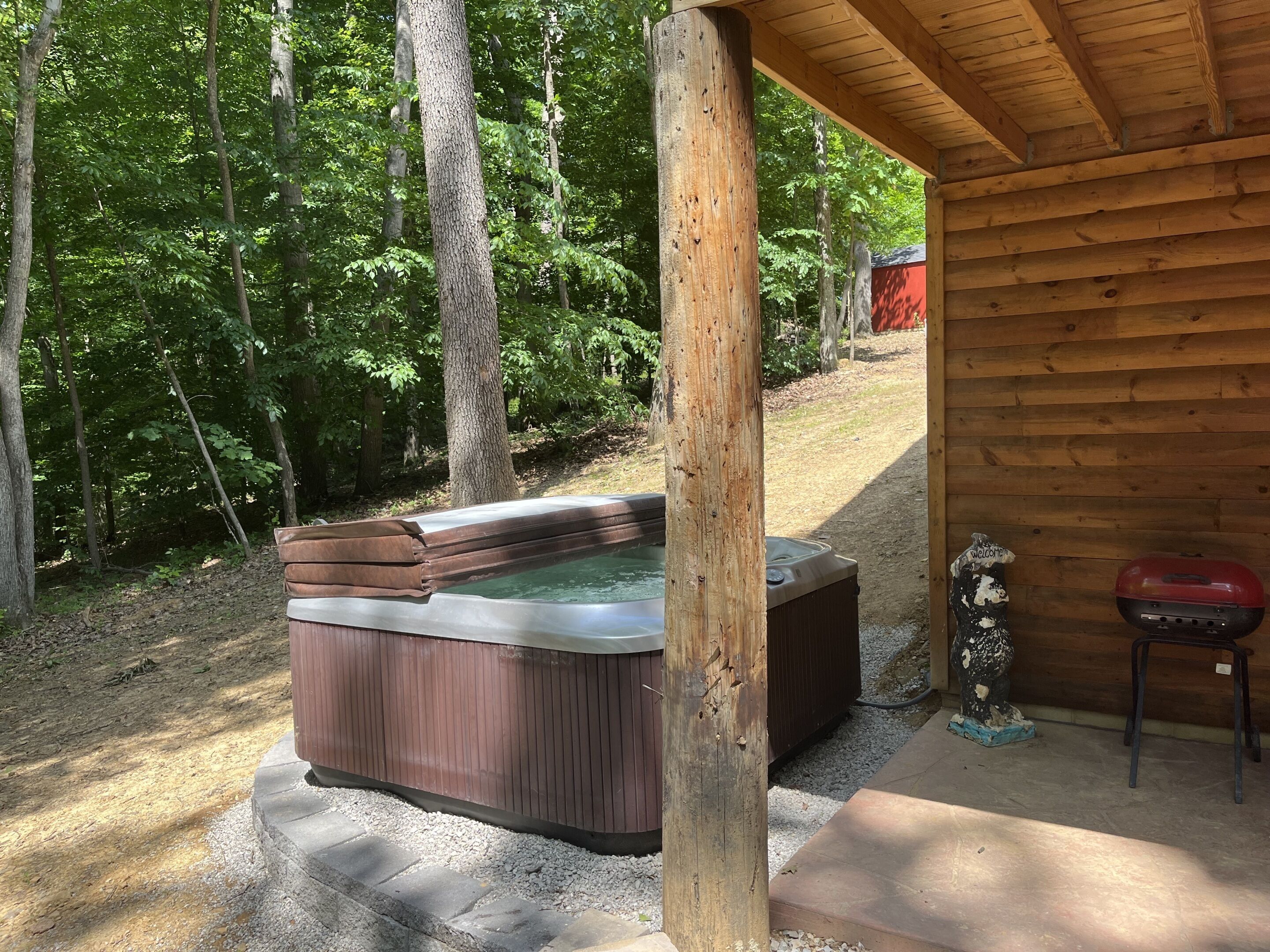 A hot tub under a wooden structure with a gravel path leading to it.