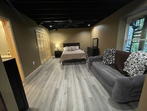 A bedroom with a bed, a sofa, a nightstand, a wardrobe, and a window. - Unique Log Cabin nestled in Forest Hocking Hills (Logan)