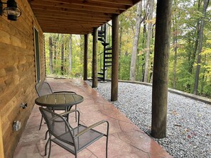 A covered outdoor seating area with a table and chairs, surrounded by trees and a gravel path. - Unique Log Cabin nestled in Forest Hocking Hills (Logan)