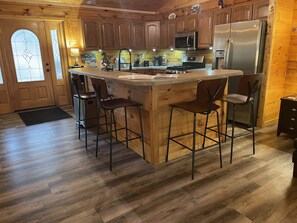 A kitchen with wooden cabinets, a stainless steel refrigerator, a microwave, and a gas stove. - Unique Log Cabin nestled in Forest Hocking Hills (Logan)