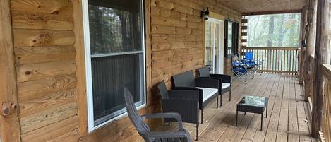 A wooden deck with outdoor furniture, including chairs and a table, and large windows.