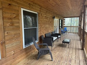 A wooden deck with wicker furniture, a glass table, and a view of the forest. - Unique Cavalier Log Cabin nestled in the forest, 15 mins to Hocking Hills (Logan)