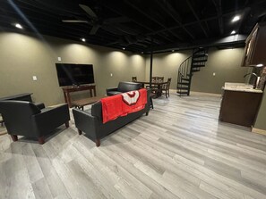 Un salón amplio con televisor de pantalla plana, un sofá con una manta roja, una mesa de comedor y una escalera que conduce a un nivel superior.