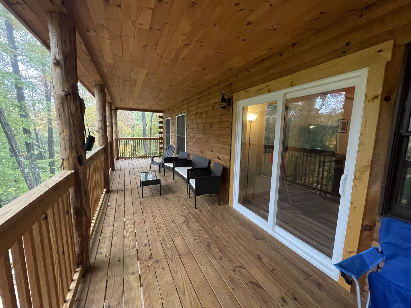 A wooden deck with a sofa and chairs, a table, and a glass door leading to an outdoor area.