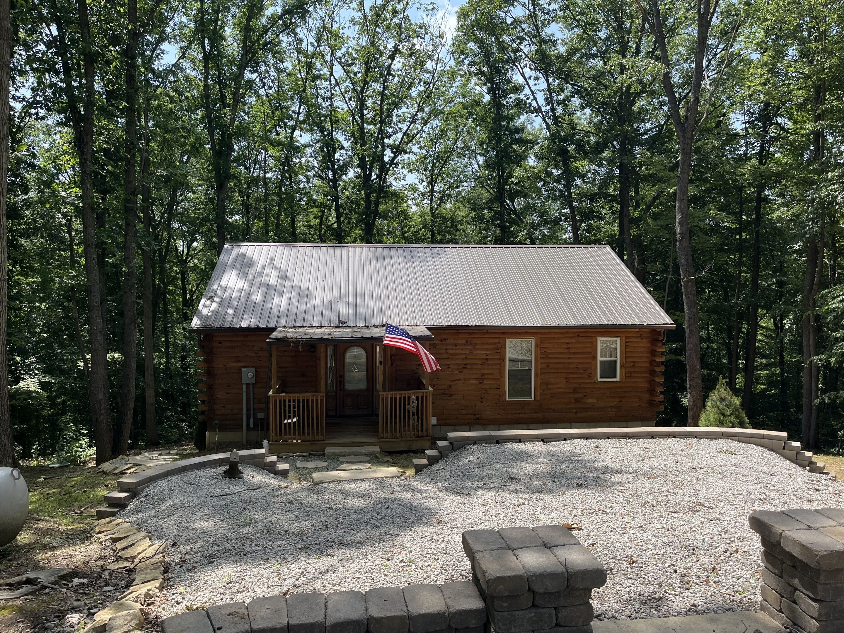 A wooden cabin with a metal roof, surrounded by a gravel driveway and a stone border.