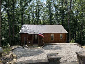 A wooden cabin with a metal roof, surrounded by a gravel area and a stone wall. - Unique Cavalier Log Cabin nestled in the forest, 15 mins to Hocking Hills (Logan)