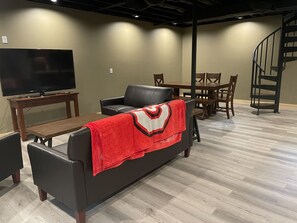 A living room with a black leather sofa, a wooden coffee table, a TV on a stand, a dining table with chairs, and a staircase. - Unique Cavalier Log Cabin nestled in the forest, 15 mins to Hocking Hills (Logan)