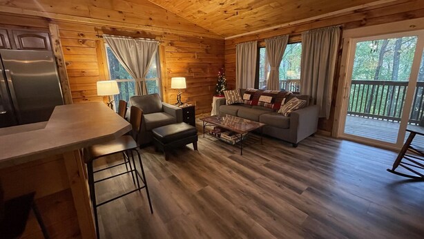A cabin interior with a dining area, sofa, and a view of the outdoors. - Unique Cavalier Log Cabin nestled in the forest, 15 mins to Hocking Hills (Logan)