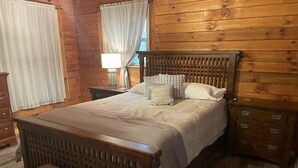 A wooden-paneled room with a bed, a nightstand, a dresser, and a bench. - Unique Cavalier Log Cabin nestled in the forest, 15 mins to Hocking Hills (Logan)