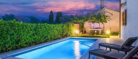 Une piscine avec des chaises longues, un patio couvert et une vue sur le ciel au crépuscule.