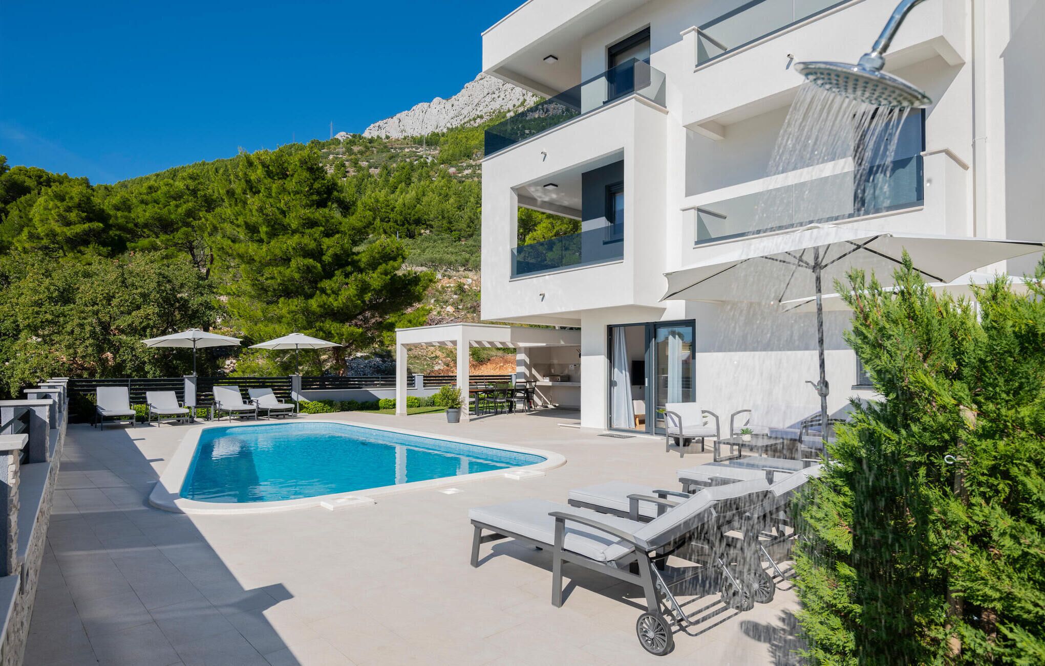 A modern two-story house with a swimming pool, outdoor seating, and a mountain backdrop.