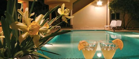 A poolside setting with a table featuring two drinks garnished with orange slices, surrounded by yellow flowers.