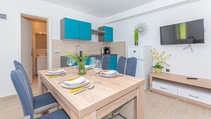 A modern kitchen with teal cabinets, a dining area with a wooden table set for four, and a TV mounted on the wall. - 1 bedroom lovely apartment in Brodarica (Brodarica)