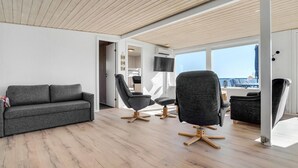 Una sala de estar moderna con un sofá gris, dos sillones negros y un techo de madera.