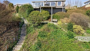 Una casa moderna con un balcón curvo, una escalera de piedra y vegetación exuberante.