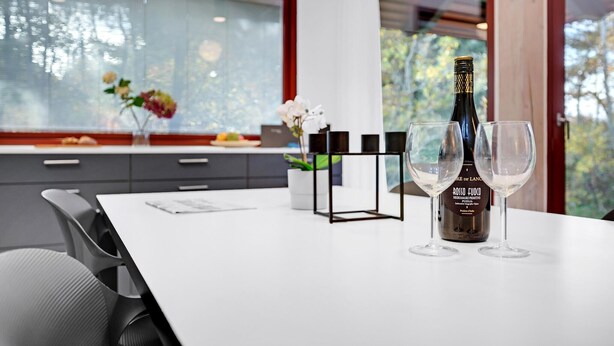Een moderne eetruimte met een witte tafel, twee wijnglazen en een fles rosso fuoco wijn.
