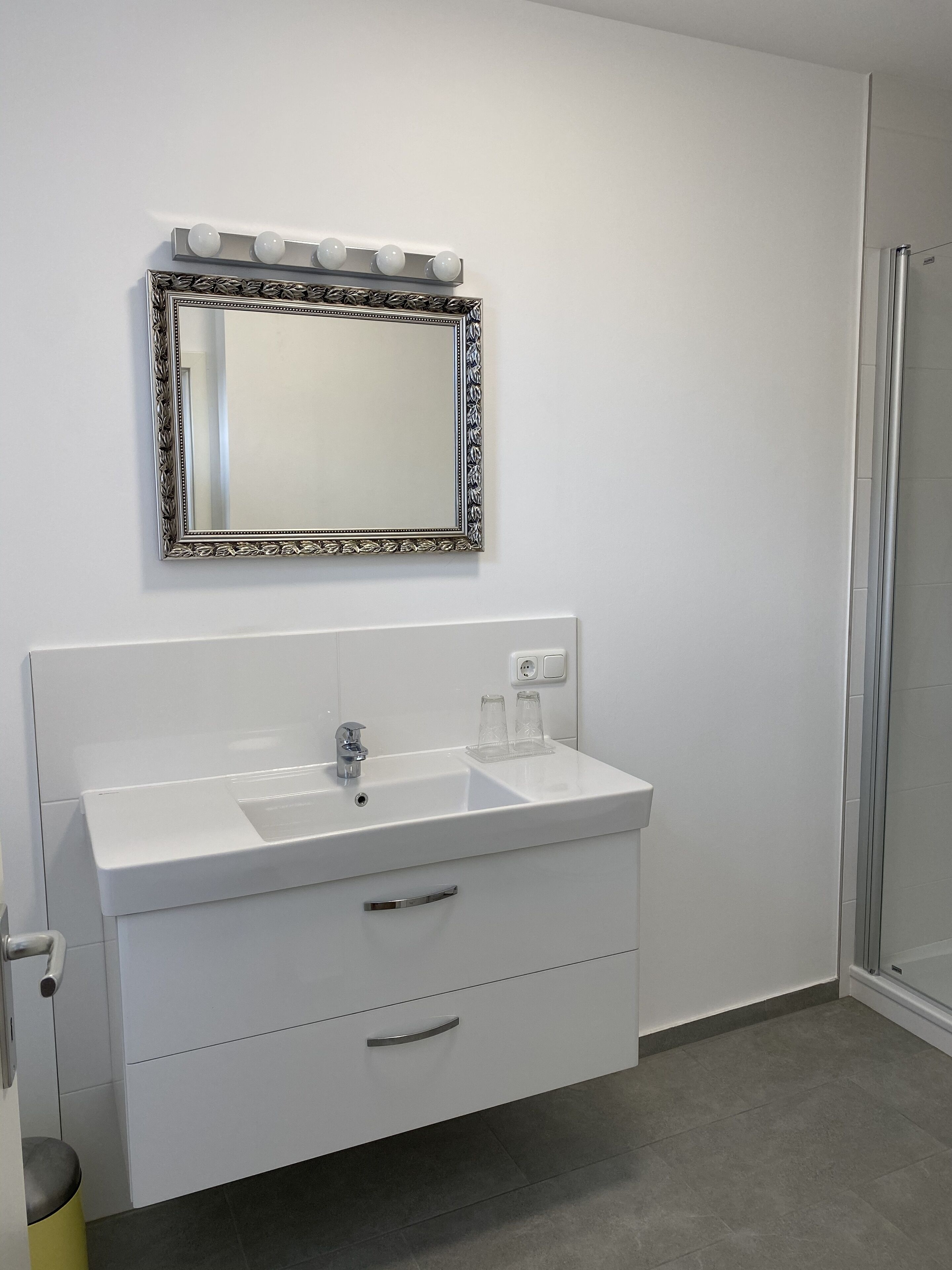 Un baño con lavamanos blanco, un espejo con marco decorativo y cabina de ducha.